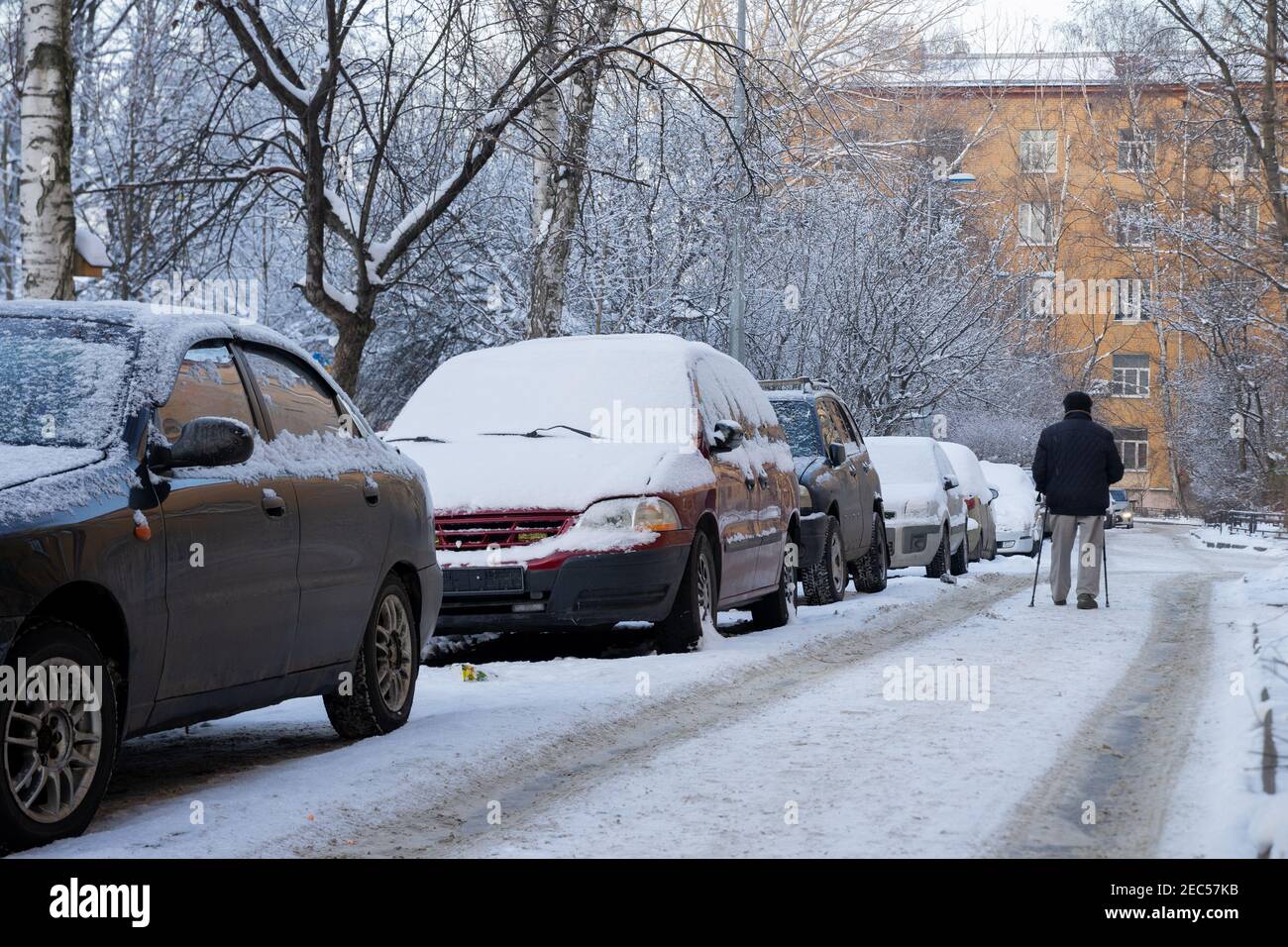 Un homme avec des bâtons de marche en hiver dans la cour vide par la rangée de voitures garées couvertes de gel frais à Saint-Pétersbourg, Russie Banque D'Images