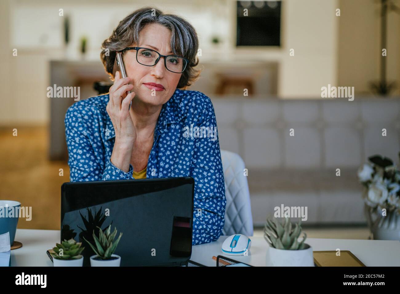 Portrait d'une femme mûre parlant sur un téléphone portable utilisant un pc portable à la maison Banque D'Images