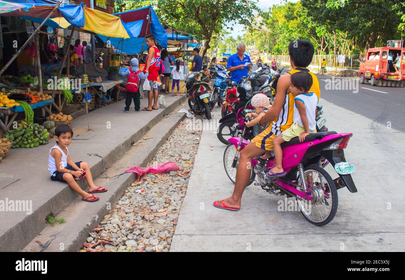 Bacong, Philippines: 26 juin, 2016: Grande famille sur moto rose par marché local. Marché alimentaire asiatique avec les habitants du village. Philippines pauvres c Banque D'Images