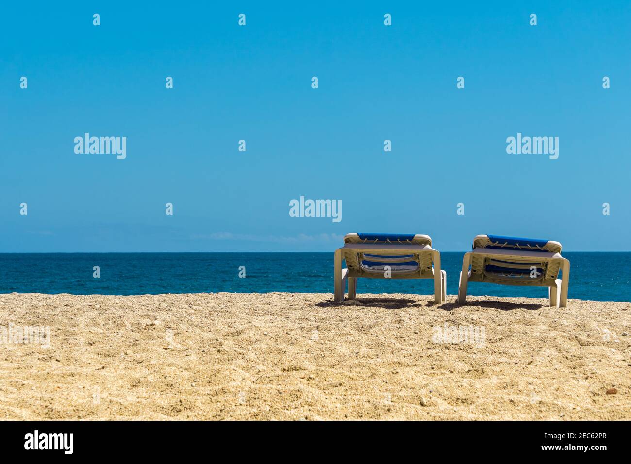 Deux chaises longues sur une plage de sable par temps ensoleillé. Chaises longues sur la côte méditerranéenne de la mer sous le ciel bleu. Banque D'Images