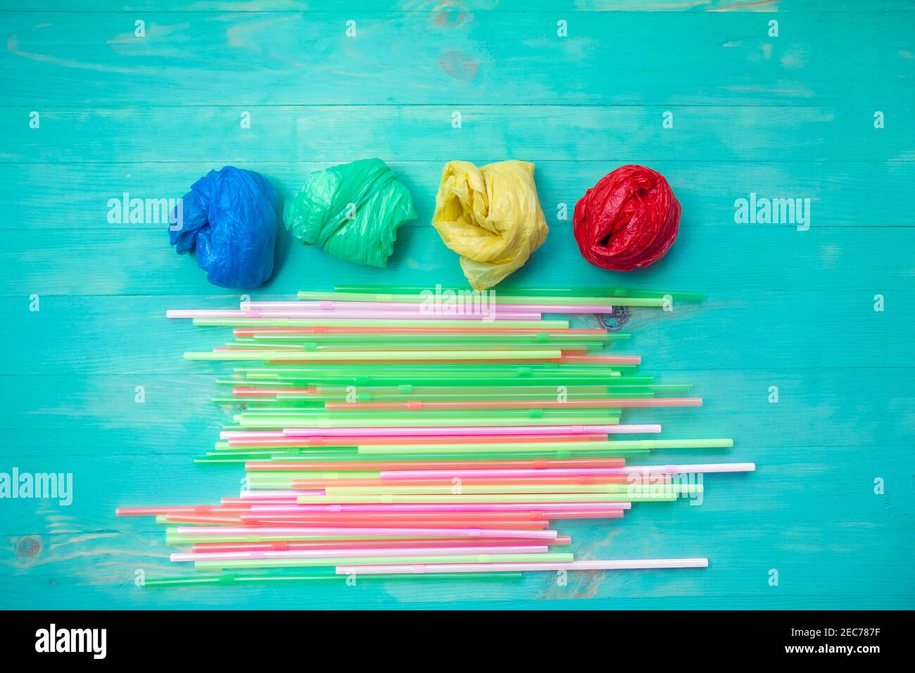 Sacs et pailles en plastique colorés sur fond turquoise en bois. Pose à plat. Concept de plastique Ban Banque D'Images