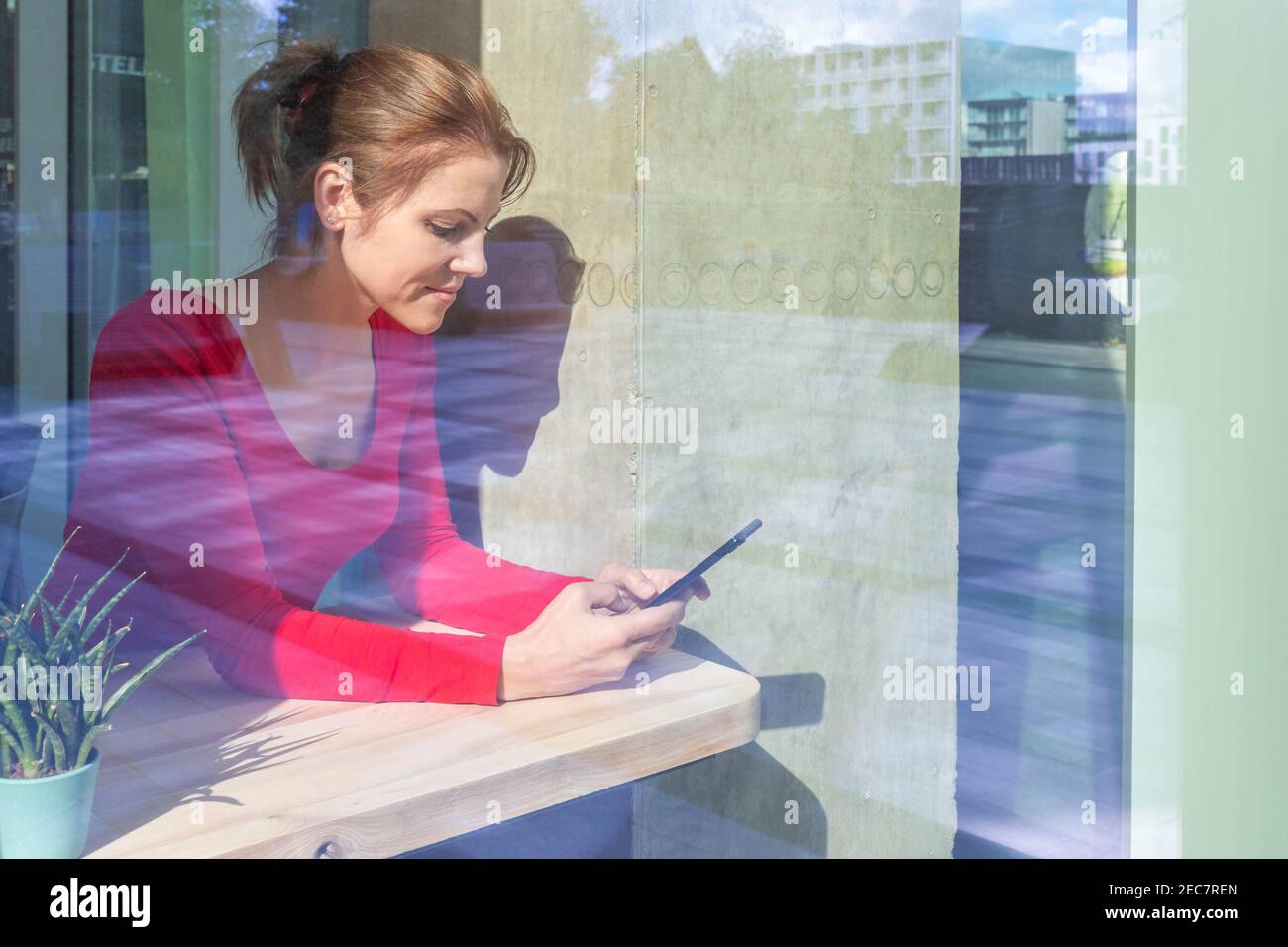 Belle femme en rouge utilisant un smartphone pour les affaires, les achats en ligne, transférer de l'argent, financier, banque sur Internet dans café-restaurant. Vue à travers W Banque D'Images