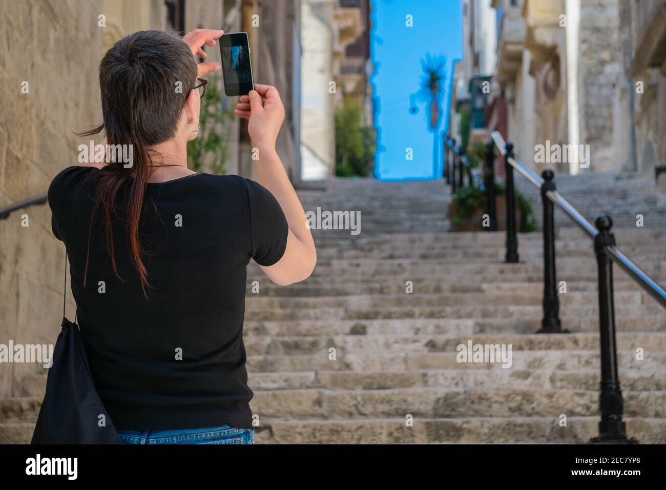 Femme prenant des photos avec un smartphone de rue étroite typique avec des escaliers et des maisons anciennes dans la ville de la Valette, la capitale de Malte, sur l'île de Malte Banque D'Images