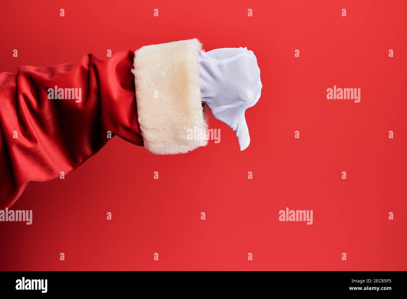 Main d'un homme portant le costume du père noël et des gants sur fond rouge faisant des pouces vers le bas geste de rejet, désapprobation et signe négatif Banque D'Images