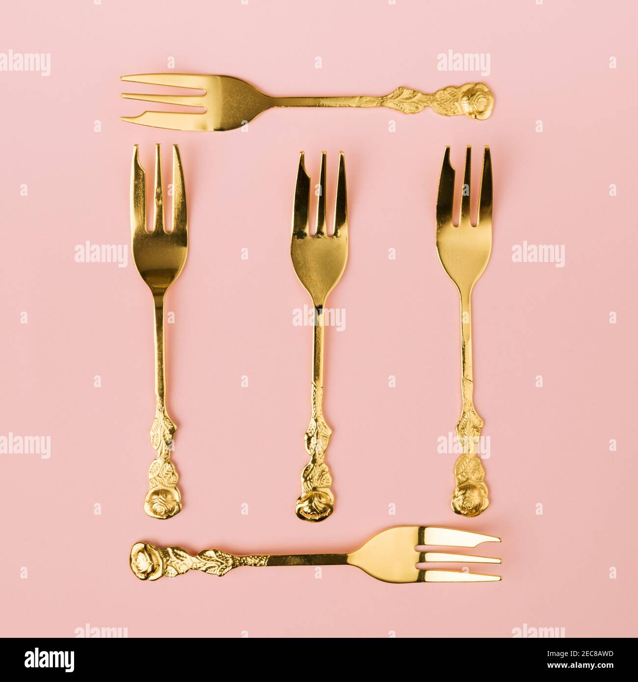 Concept créatif minimal de fourchettes en or faisant un symbole carré avec un fond rose pastel agréable. Idée de célébration Banque D'Images