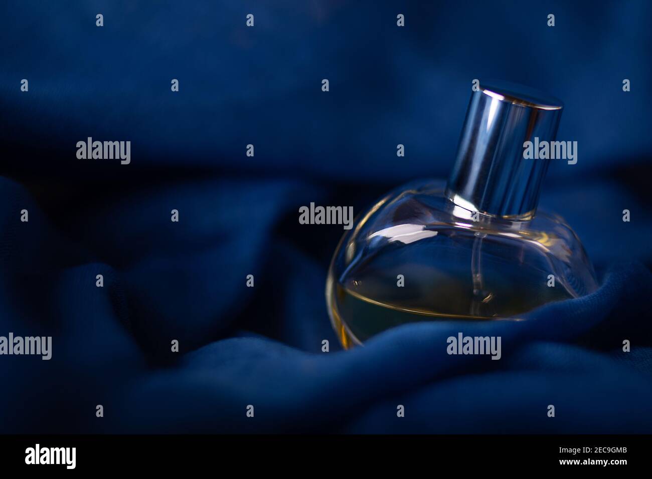 Bouteille de parfum en verre sur fond bleu foncé romantique mystérieux. Concept de senteurs et odeurs gros plan macro studio tourné avec l'espace de copie. Banque D'Images