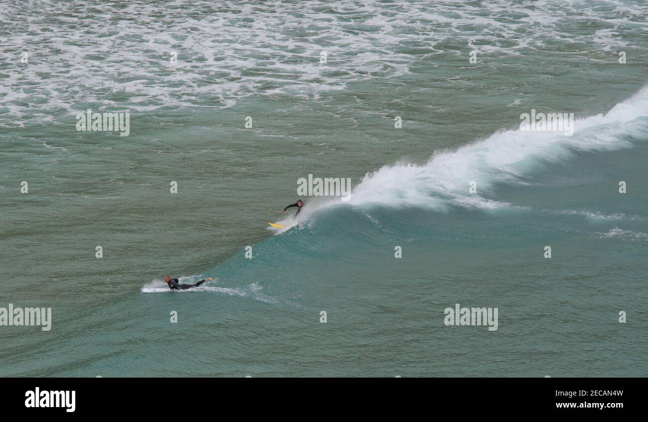 Les surfeurs attrapent une vague au large de la plage de Porthcurno, Penwith Peninsula, Cornouailles Banque D'Images