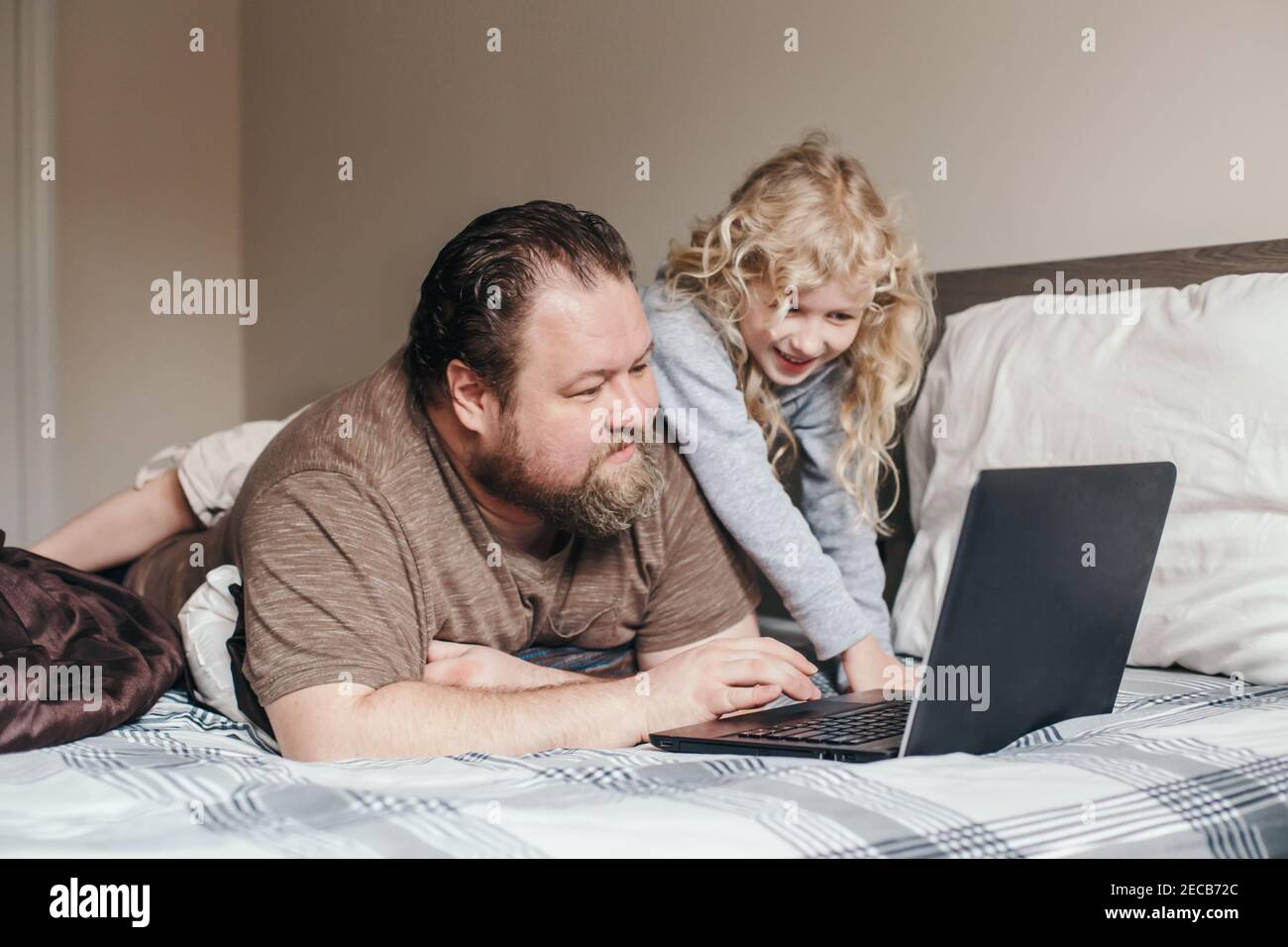 Travaillez à la maison avec des enfants. Père travaillant sur un ordinateur portable dans la chambre avec l'enfant fille sur son dos. Un moment de famille drôle et sincère. Nouvelle normale pendant Banque D'Images