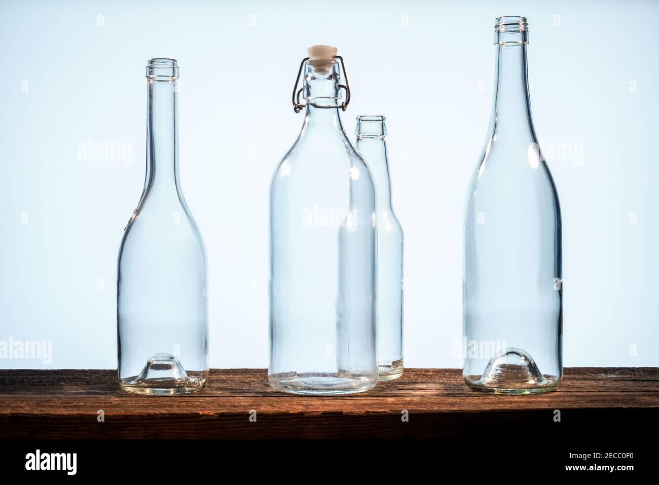 Quatre bouteilles en verre transparent sur une table en bois de grange avant d'un arrière-plan blanc Banque D'Images