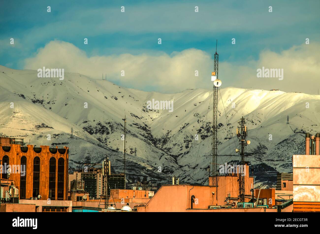 Montagnes Tochal enneigées contre un ciel bleu avec des nuages épais Au pied de la ville densément construite de Téhéran Banque D'Images