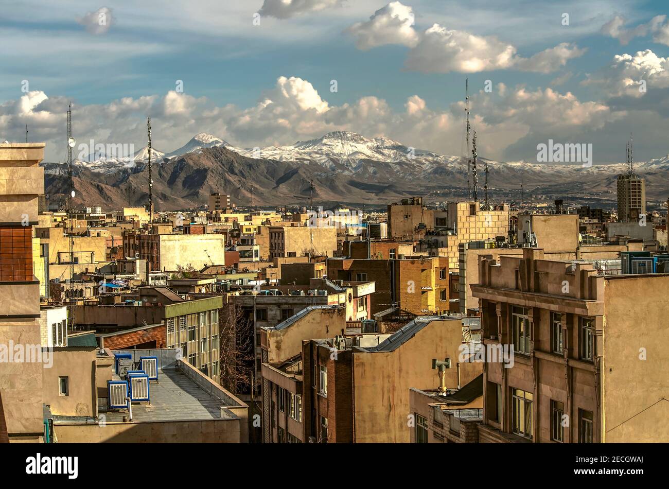Les toits d'un Téhéran étroitement construit entouré par les montagnes ont été enneigées contre un ciel bleu avec des nuages épais Banque D'Images