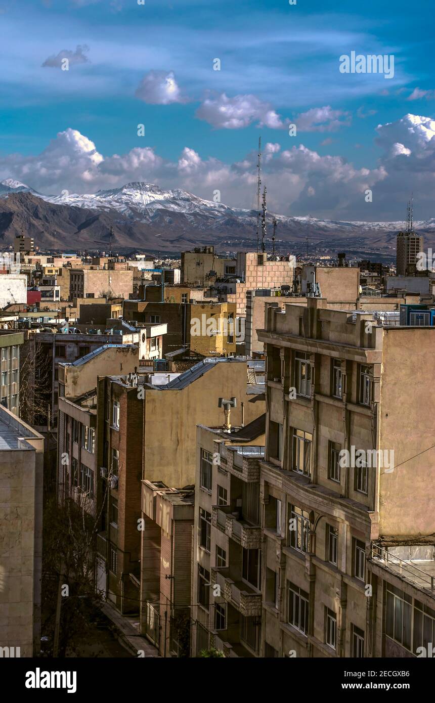 Vue sur les toits de Téhéran densément peuplés contre le ciel bleu avec nuages et montagnes enneigées Banque D'Images