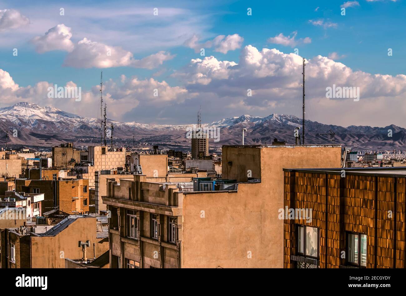Vue sur les toits plats de Téhéran très bien construits à le pied des montagnes enneigées contre un ciel bleu avec nuages épais Banque D'Images