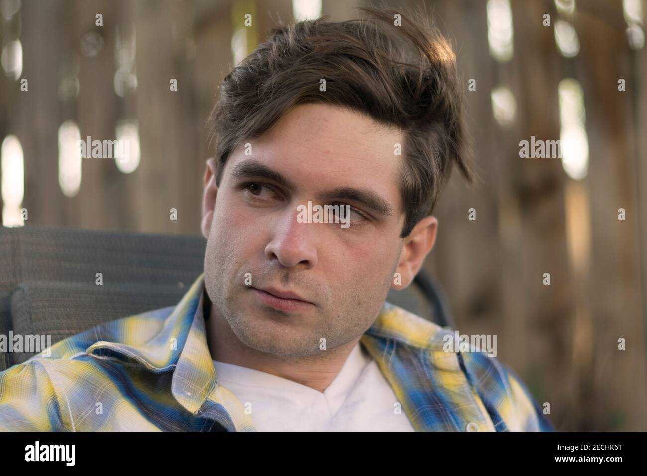 Un jeune homme a une expression sérieuse sur son visage tout en se relaxant à l'extérieur à l'ombre. Banque D'Images