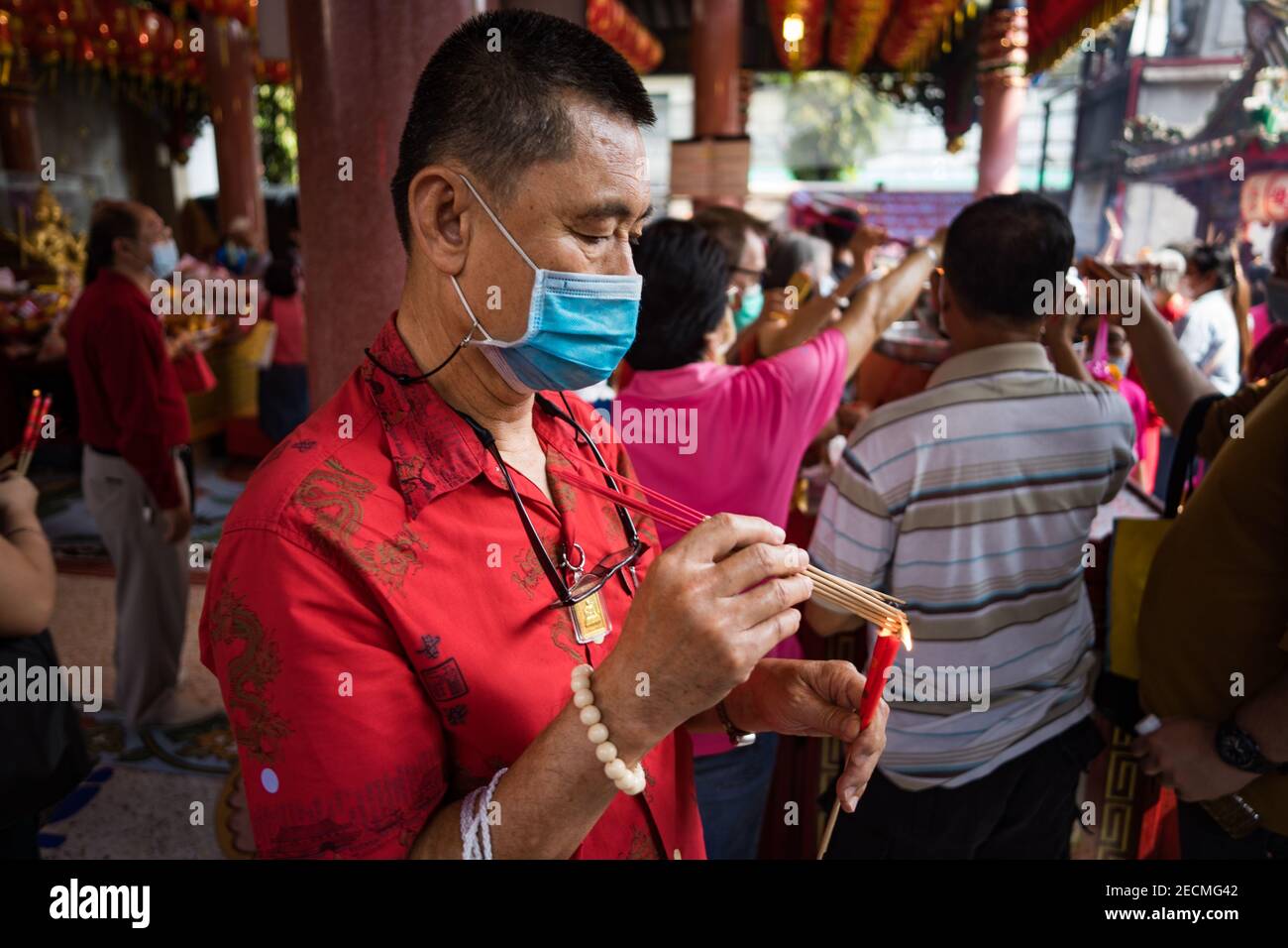 Homme en masque éclairant l'encens à une pagode de Bangkok Pendant le nouvel an chinois Banque D'Images