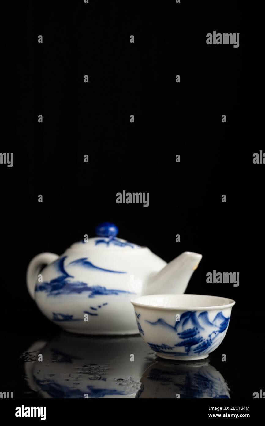 gros plan de la théière et de la tasse en porcelaine bleue, sur une surface avec reflet, sur fond noir, à la verticale, avec espace de copie Banque D'Images