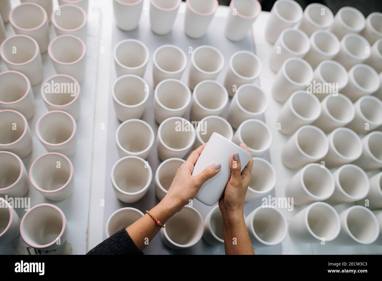 Femme mains tenant la tasse au-dessus des rangées de tasses vierges sur une table dans une salle de stockage Banque D'Images
