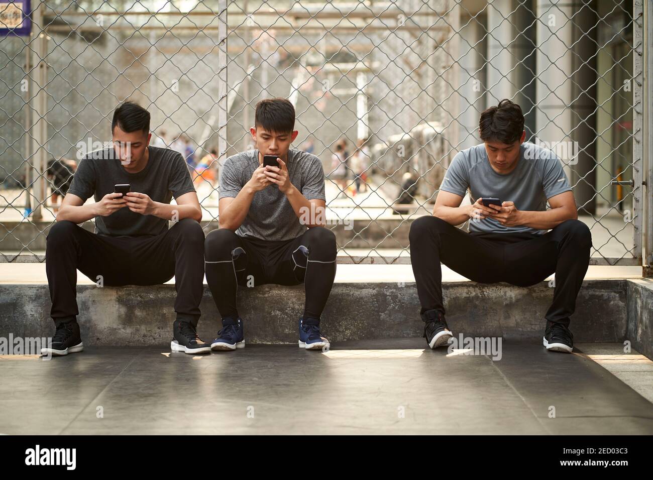 trois jeunes hommes adultes asiatiques assis sur le sol regardant téléphone mobile extérieur Banque D'Images