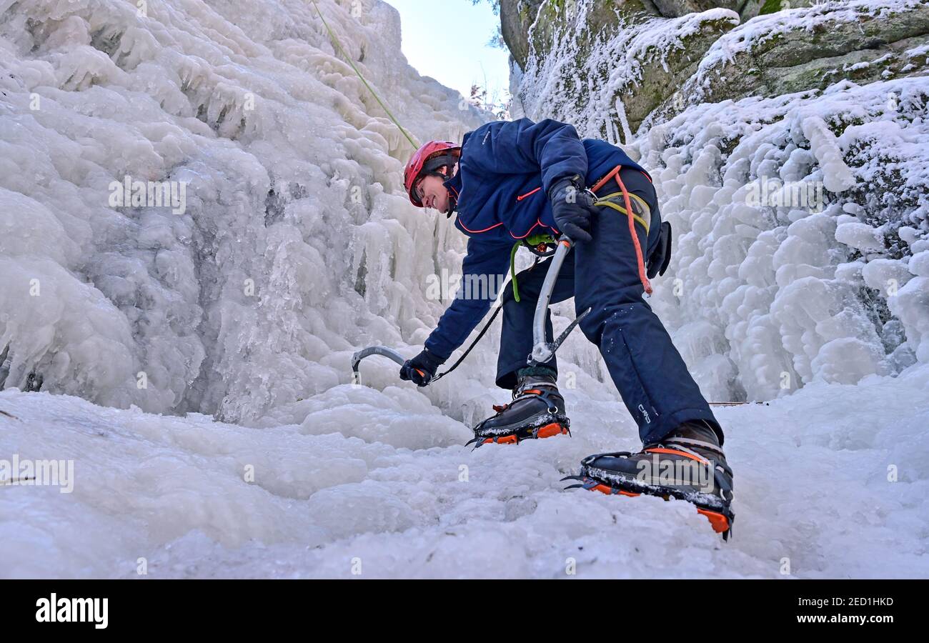 Eibenstock, Allemagne. 14 février 2021. Bien équipée avec des crampons et une hache à glace et fixée par corde, une femme monte dans la chute d'eau glacée Blauenthal. Les températures glaciales actuelles ont transformé la cascade de près de 30 mètres de haut en un mur de glace. L'endroit idyllique n'est pas seulement populaire auprès des amateurs d'escalade. Beaucoup ont profité du beau temps au week-end pour un voyage dans la région autour d'Eibenstock. Credit: Hendrik Schmidt/dpa-Zentralbild/ZB/dpa/Alay Live News Banque D'Images