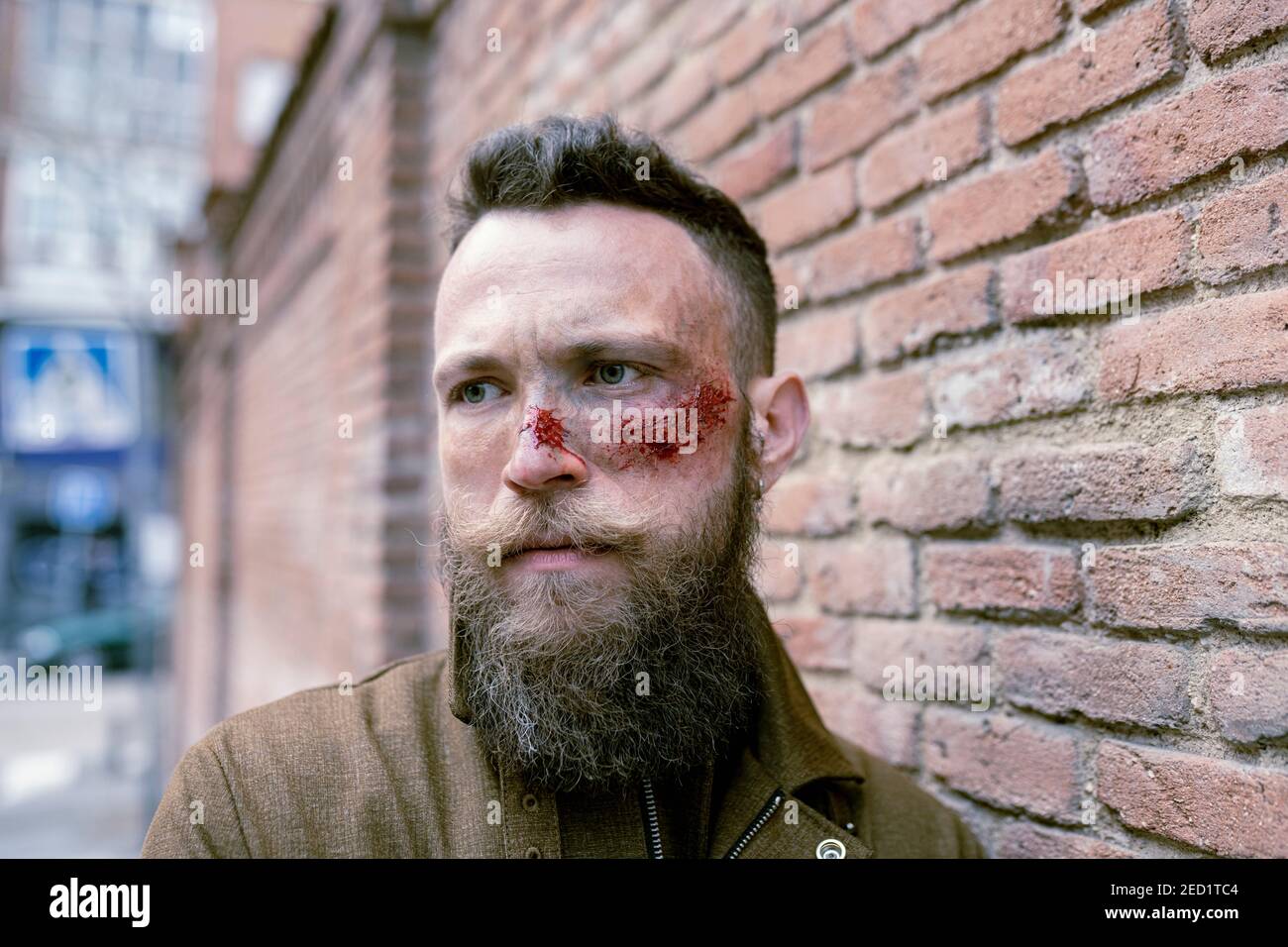 Vue latérale de l'homme hippster avec la barbe et le maquillage de cinéma posant dans la rue Banque D'Images