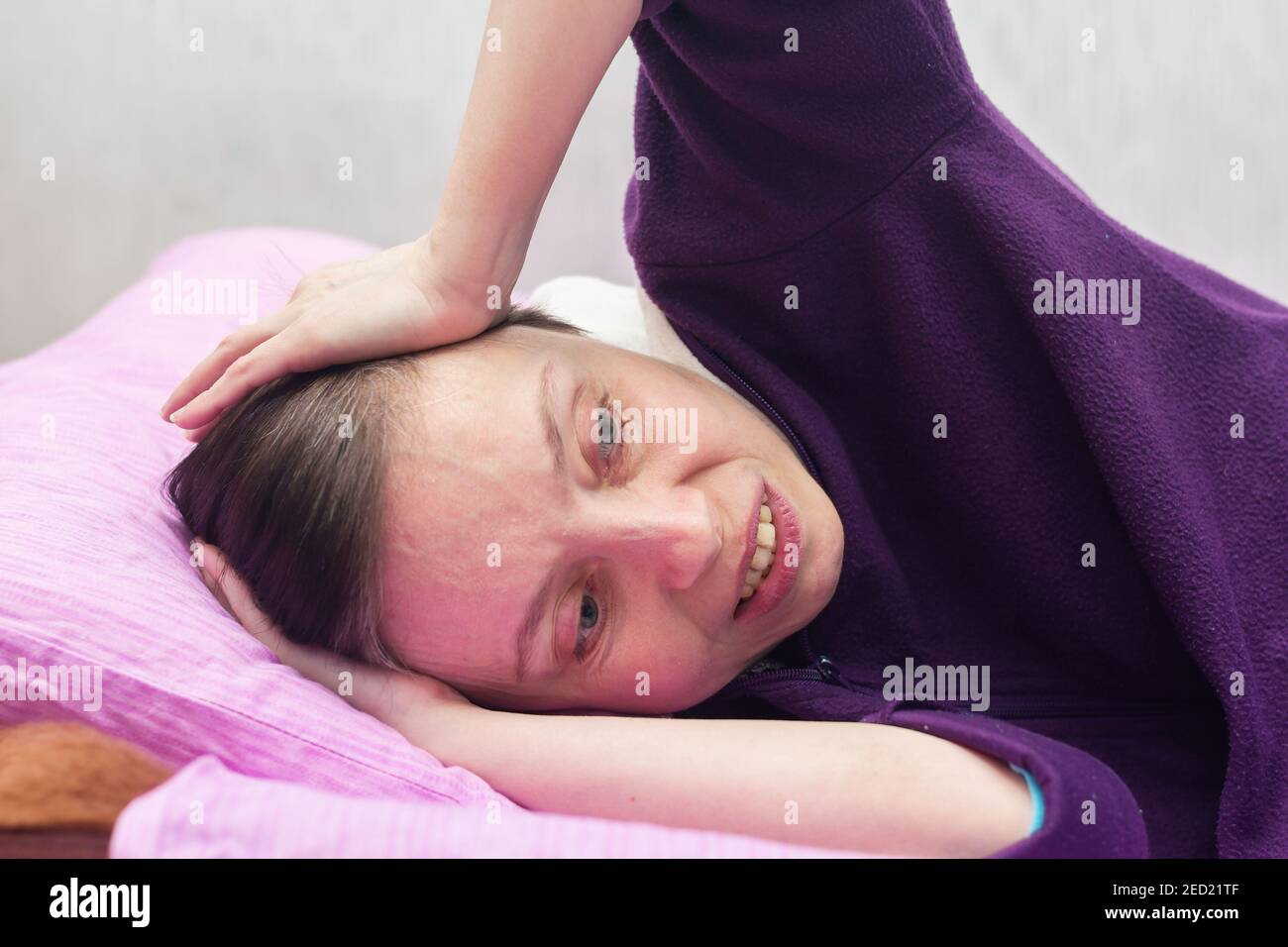 La femme se trouve sur le lit et souffre d'un mal de tête sévère. Banque D'Images