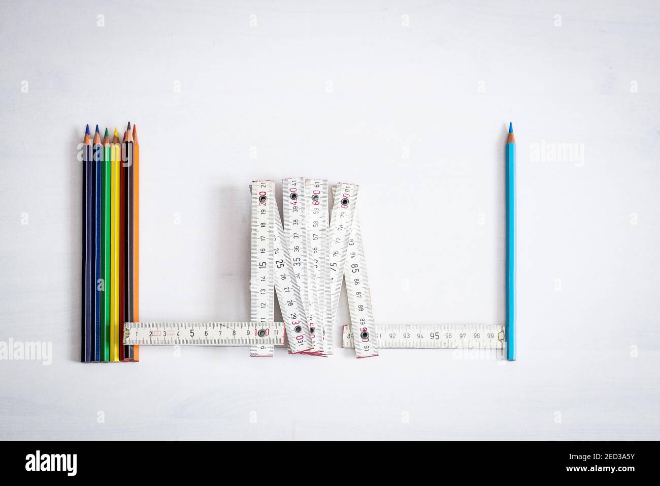 Groupe de crayons de couleur espacés par un seul crayon avec un mètre en bois, le concept de distance sûre dans les salles de classe pour éviter la contagion. Banque D'Images