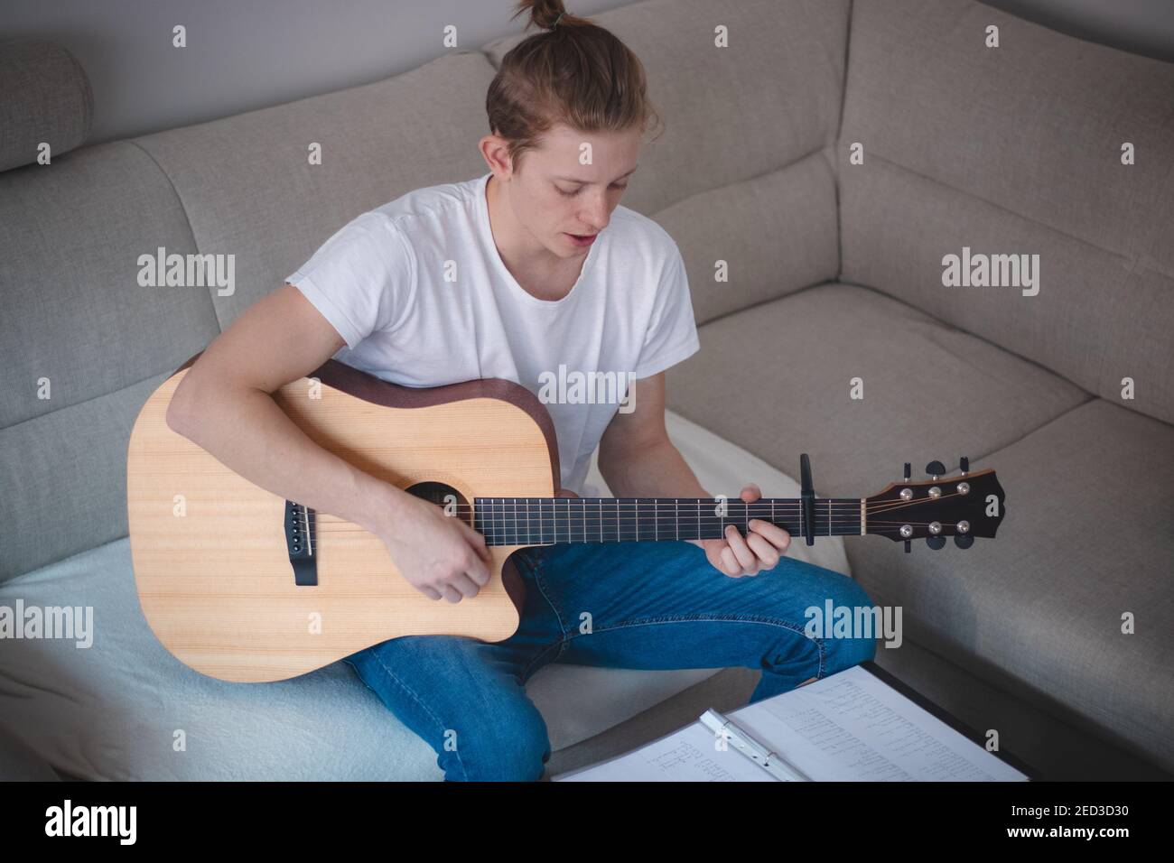 Portrait franc d'un jeune chanteur jouant une guitare acoustique et chantant dans un livre d'hymne dans un salon éclairé aux tons gris. Une expérience magnifique. Banque D'Images
