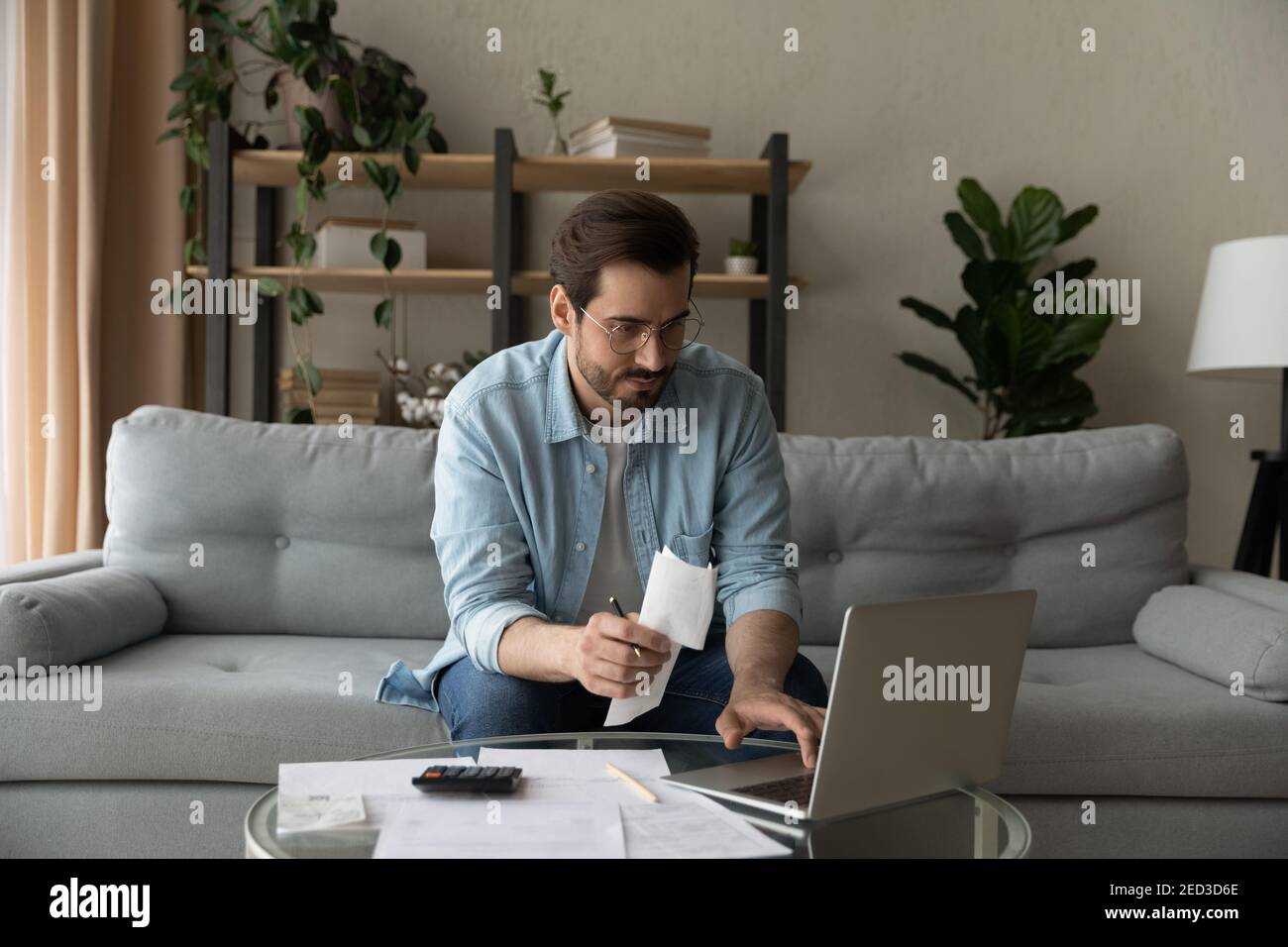 Un homme millénaire sérieux s'est concentré sur le paiement des factures d'électricité à l'aide d'un ordinateur portable Banque D'Images
