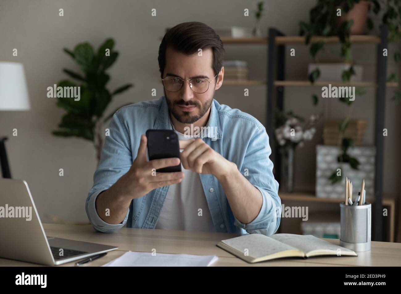 Un jeune étudiant sérieux vérifie des informations incertaines en ligne à l'aide d'un smartphone Banque D'Images