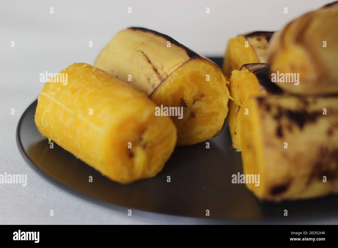 Plantain mûr cuit à la vapeur et servi sur une assiette de taille moyenne gris foncé. Prise de vue sur fond blanc Banque D'Images