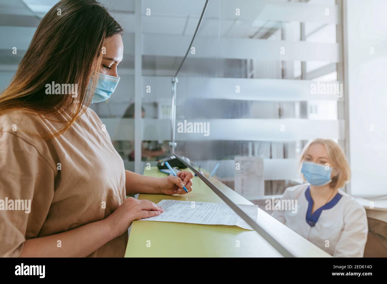 Une infirmière ou un médecin expliquant au patient comment remplir le formulaire médical à la réception de l'hôpital. Médecin et patient portant des masques de protection et utilisant p Banque D'Images