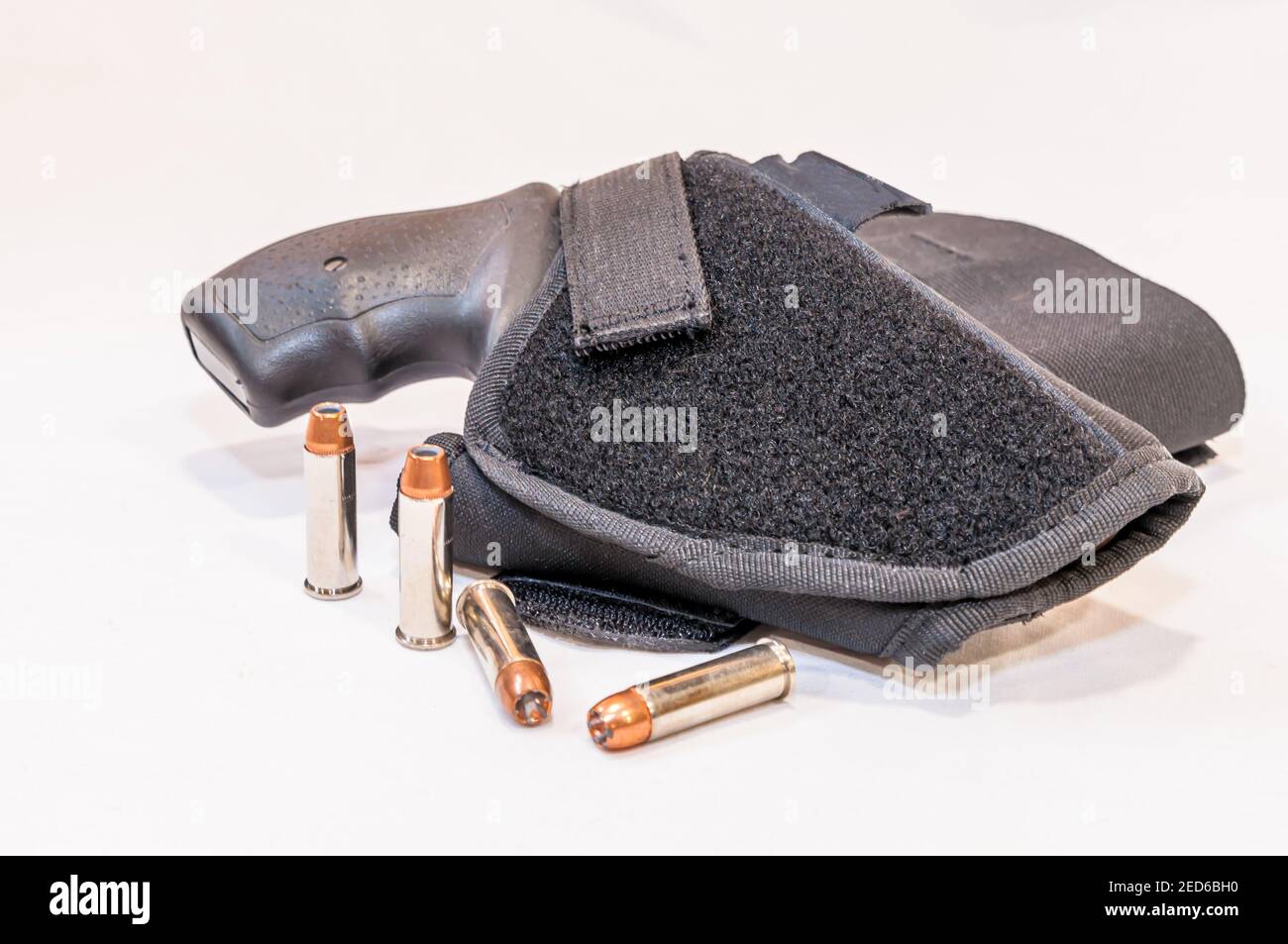 Un revolver spécial 38 noir à nez à priser dans un chiffon étui avec quatre puces à pointe creuse à côté un arrière-plan blanc Banque D'Images