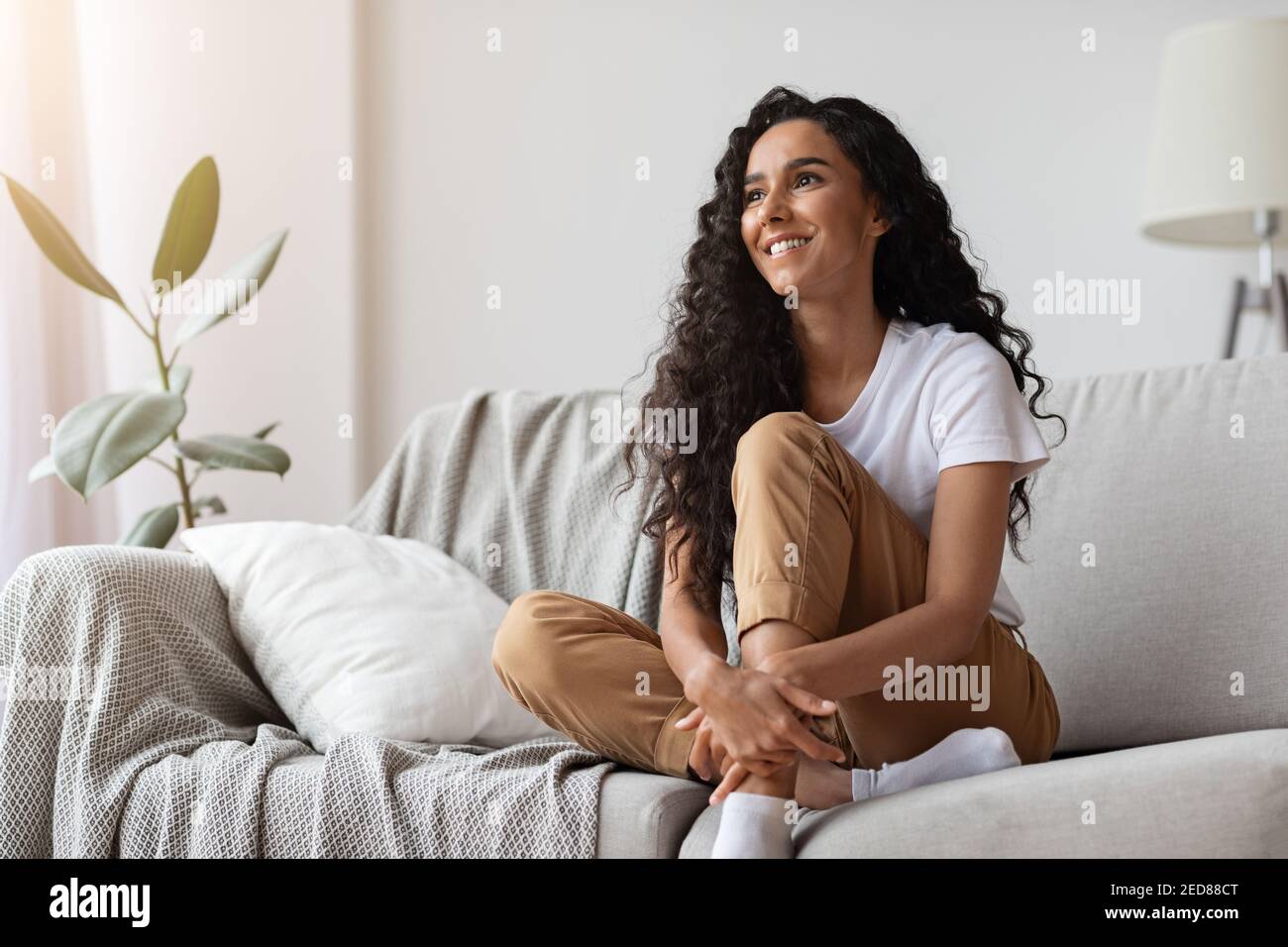 Jeune femme joyeuse assise sur un canapé à la maison Banque D'Images