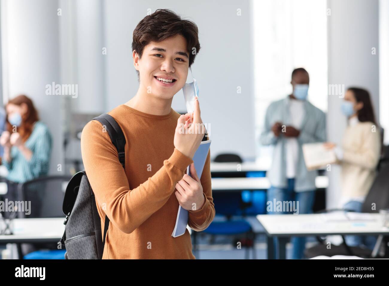 Un homme asiatique souriant prend un masque médical jetable en classe Banque D'Images