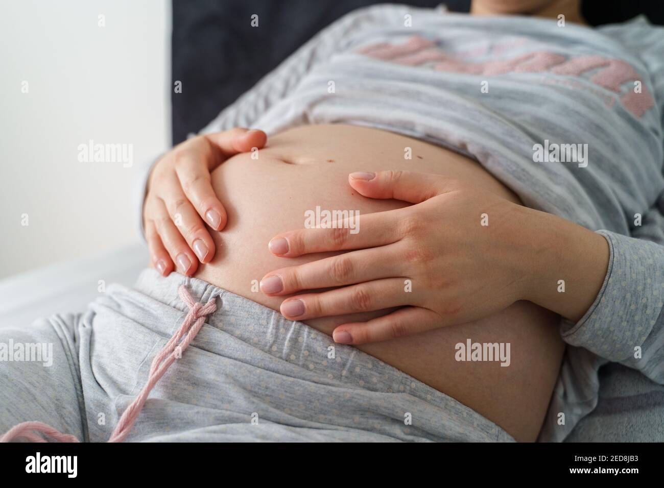 Vue latérale sur la section médiane de la femme blanche enceinte allongée le lit avec lit tenant le ventre - grossesse concept Banque D'Images
