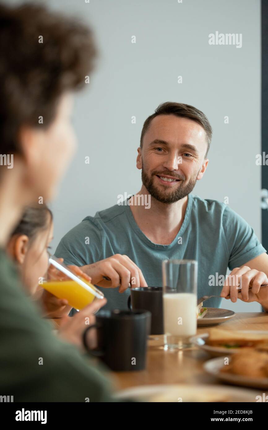 Un jeune homme souriant prend le petit déjeuner à côté de la table du dîner et regarder sa femme tout en l'écoutant pendant la discussion de plans pour la journée Banque D'Images