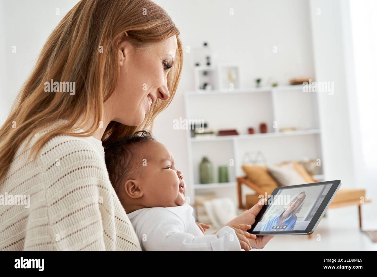 Mère caucasienne tenant bébé africain pleurant ayant la réunion appel vidéo à la maison. Banque D'Images