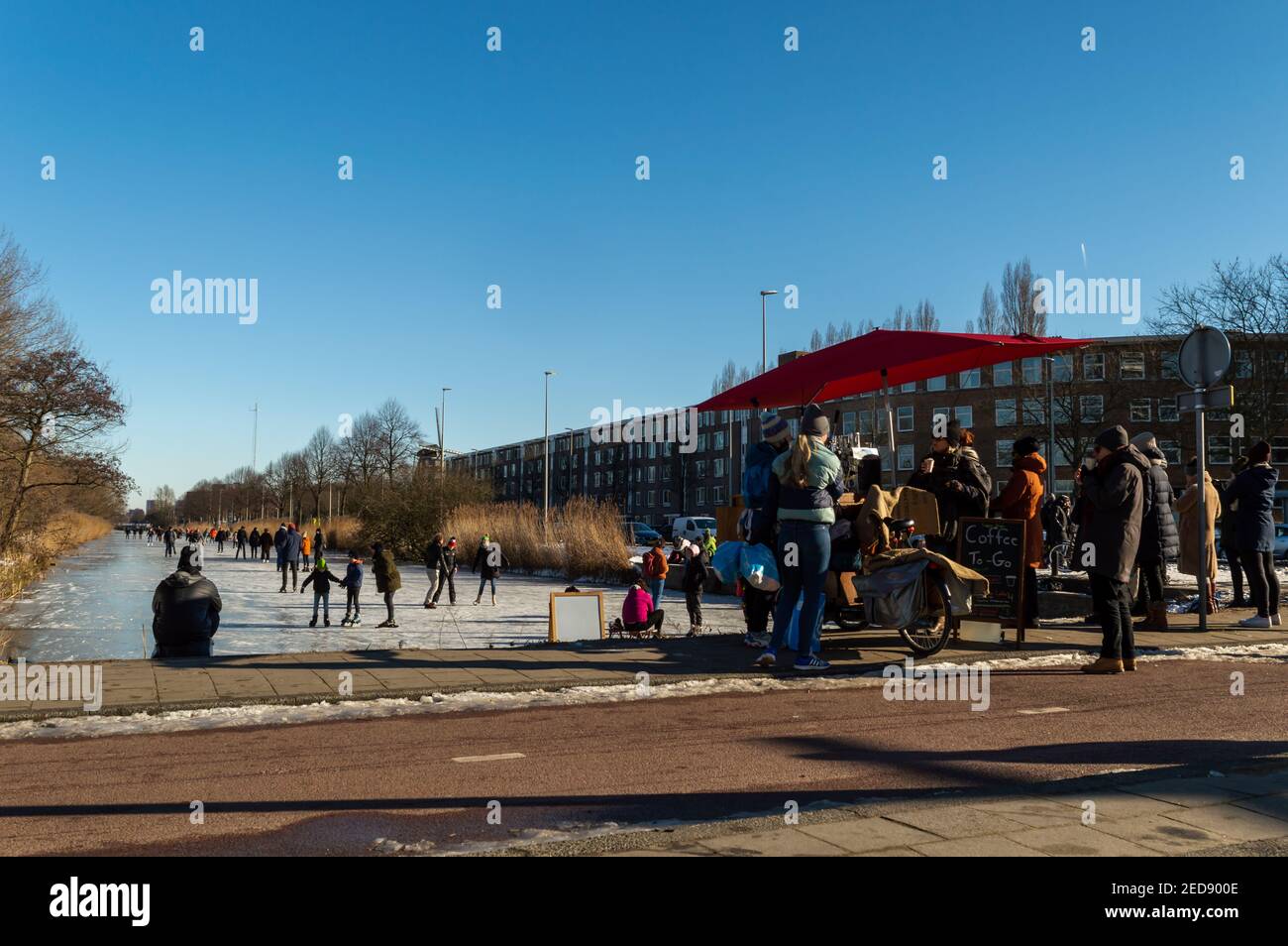 AMSTERDAM, PAYS-BAS, FÉVRIER 13,2021. Les gens patinent sur le canal gelé de Haarlemmerweg à Amsterdam et un café de rue avec Banque D'Images