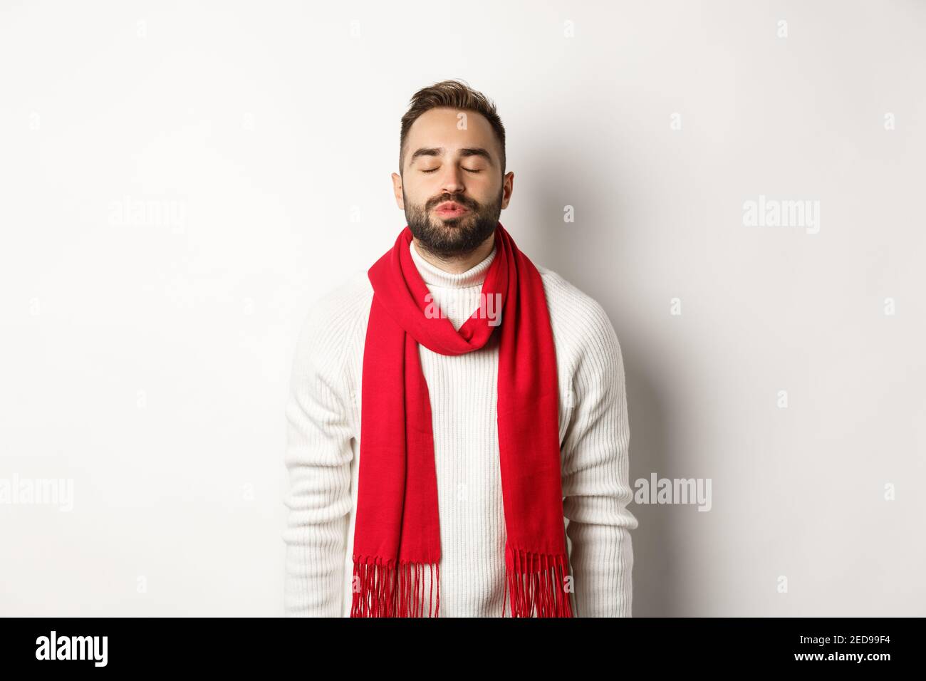 Beau homme debout avec les yeux fermés et les lèvres puckées, attendant le  baiser de noël sous le GUI, debout sur fond blanc en foulard d'hiver Photo  Stock - Alamy