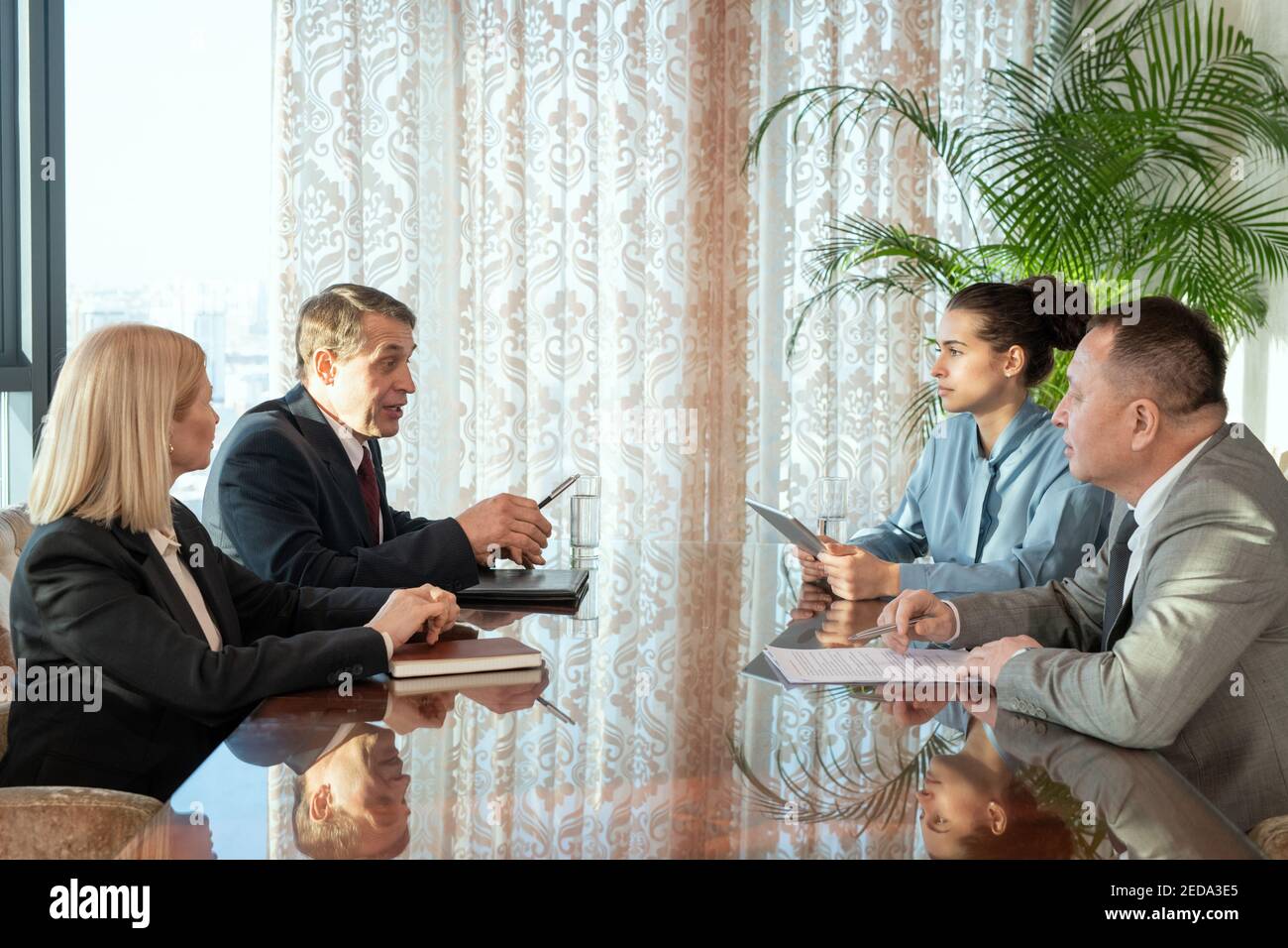 Des délégués masculins matures et leurs secrétaires élégants discutent des termes et conditions du contrat pendant la négociation lors d'une réunion dans la salle de réunion Banque D'Images