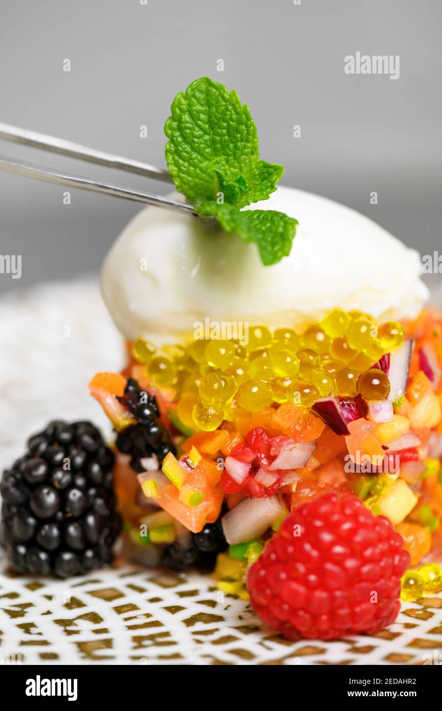 Vue rapprochée d'un chef de cuisine fine plaçant un congé de menthe sur le plat servi avec des pinces de cuisine tout en le décorant. Photo de haute qualité. Banque D'Images