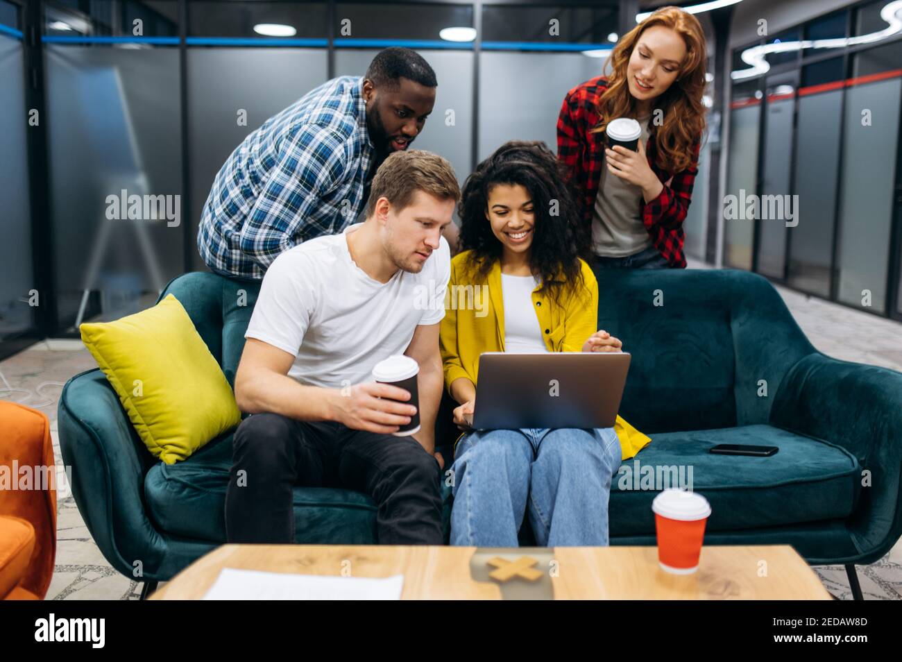 Des jeunes employés adultes heureux en pause, boivent du café, parlent du processus de travail. Collègues amicaux utilisant un ordinateur portable, discutant du projet, recherchant des idées de démarrage. Concept de communication Banque D'Images