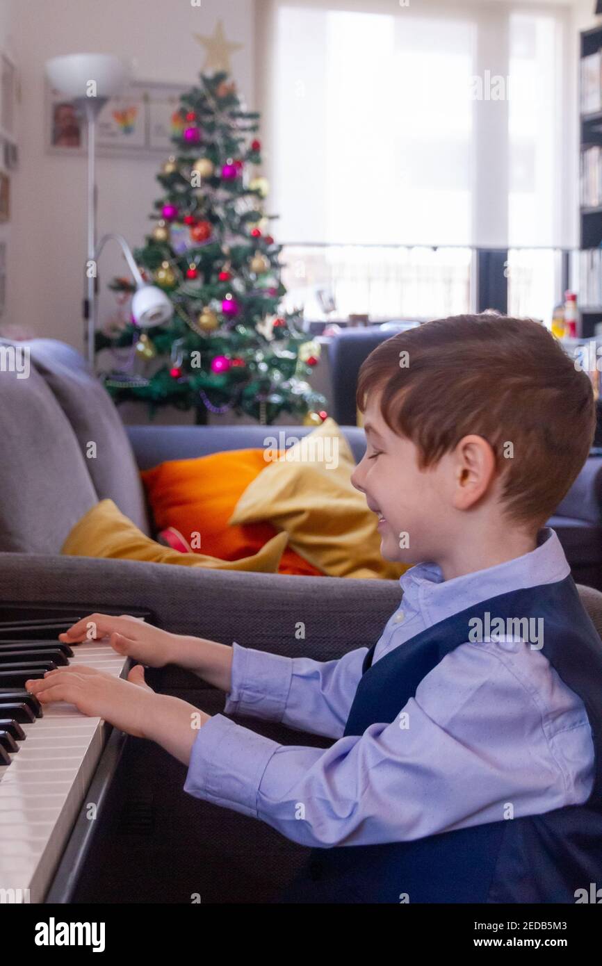 Garçon jouant du piano dans un salon avec un Arbre de Noël en arrière-plan Banque D'Images