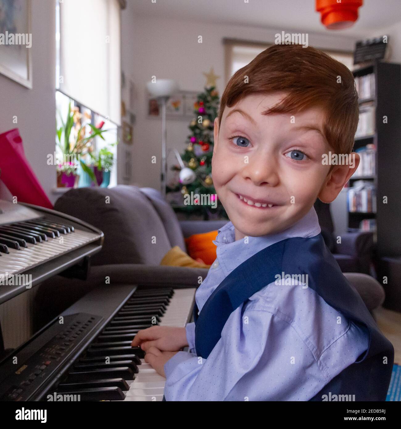 Garçon jouant du piano dans un salon avec un Arbre de Noël en arrière-plan Banque D'Images