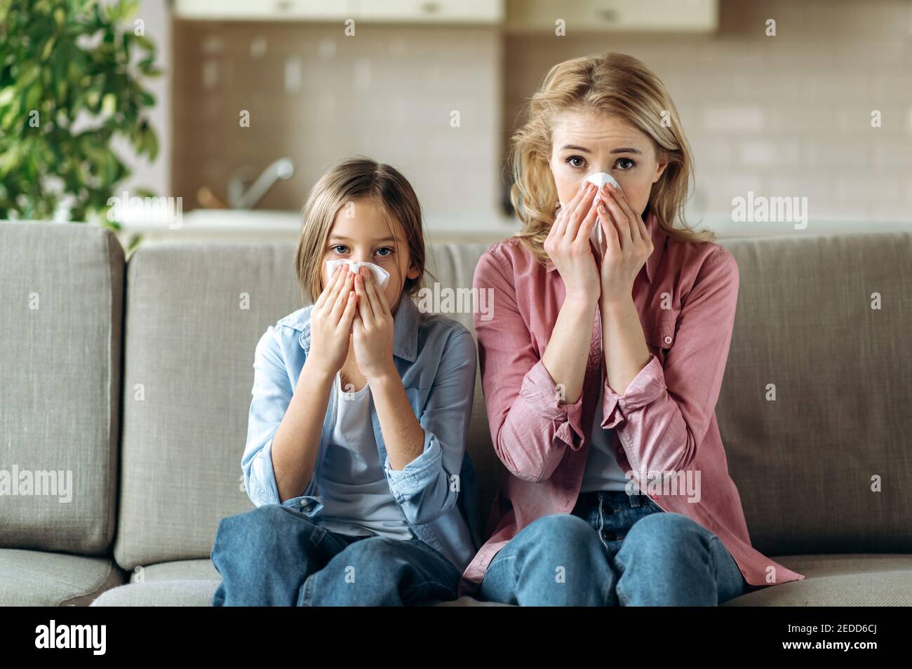 Triste mère caucasienne et fille avec un rhume sont assis à la maison sur le canapé avec des serviettes, éternuer, toux, nez qui coule. Rhume, grippe, maladie Banque D'Images