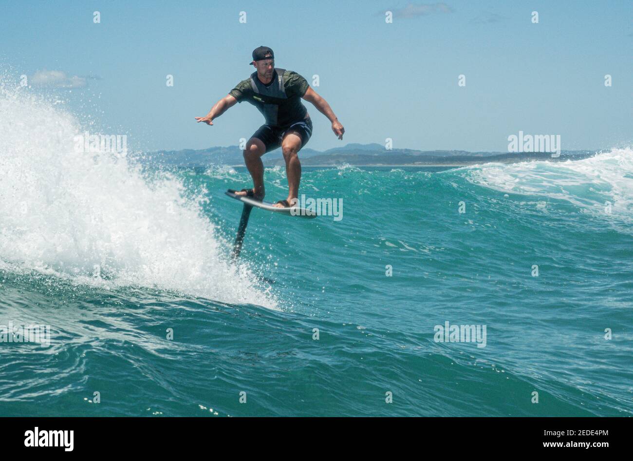 Un homme surfe sur une planche de surf hydrofoil sur des vagues turquoise à Mangawhai Heads, en Nouvelle-Zélande. Ciel bleu clair. Banque D'Images