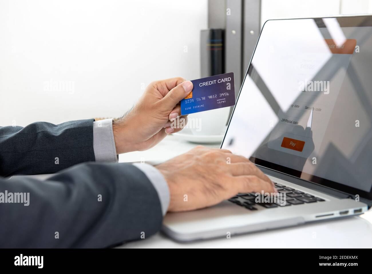 Main de l'homme d'affaires tenant la carte de crédit faisant la transaction de paiement en ligne avec ordinateur portable au bureau Banque D'Images