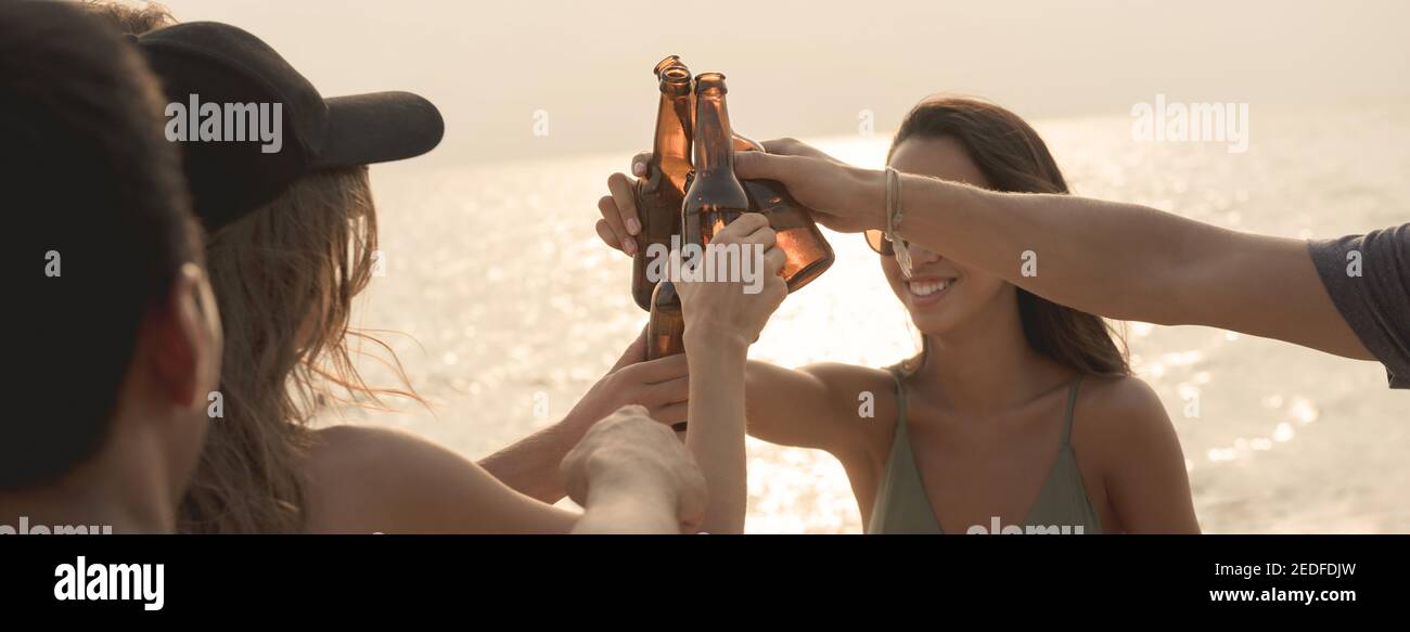 Groupe d'amis qui ont la fête de célébration de la mise en bouteilles de bière faire un toast avant de boire à la plage au crépuscule, bannière panoramique Banque D'Images