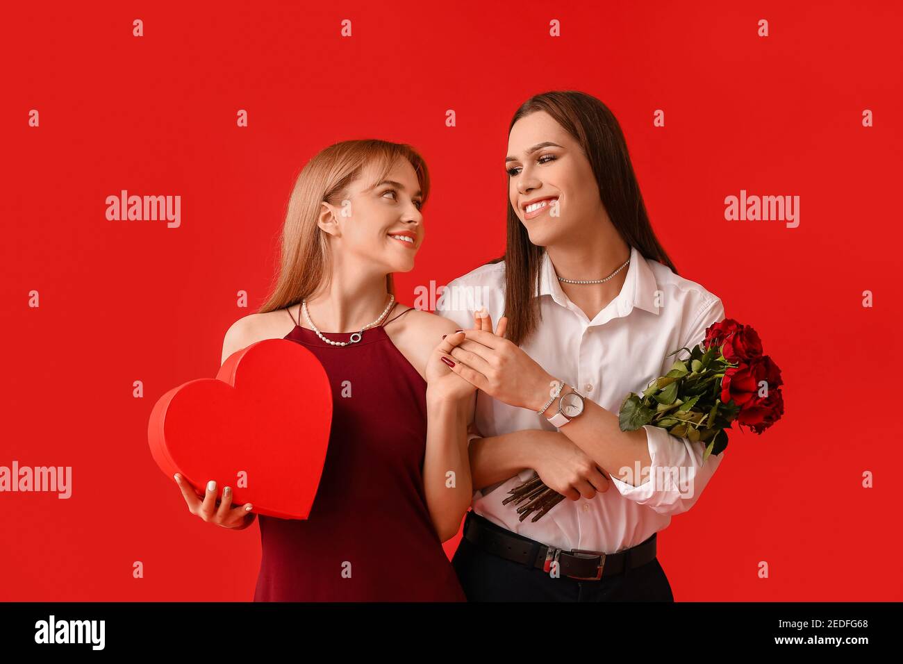 Jeune couple transgenre avec fleurs et cadeau sur fond de couleur.  Célébration de la Saint-Valentin Photo Stock - Alamy