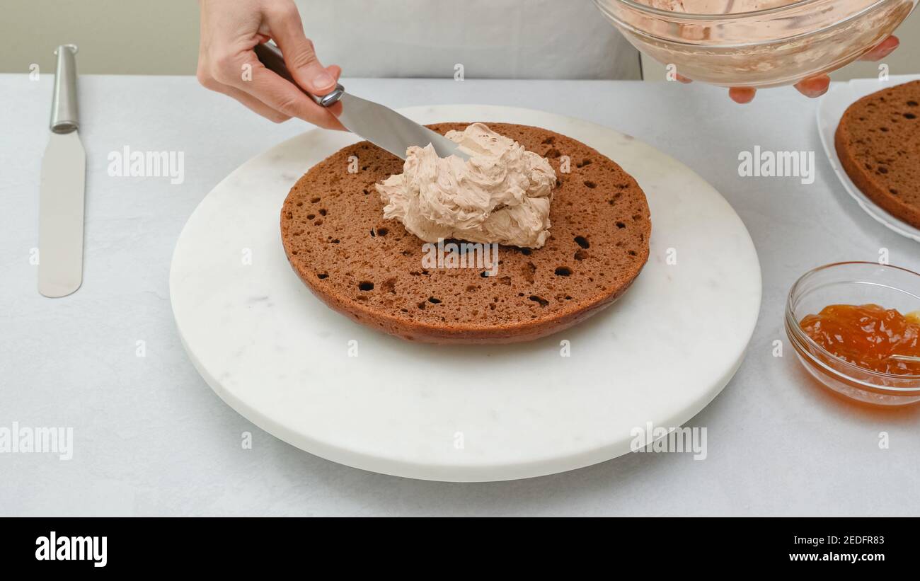 Assemblage du gâteau au chocolat. Chef plaçant le glaçage au gâteau au chocolat sur la première couche. Recette de gâteau au chocolat étape par étape Banque D'Images